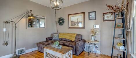 A cozy living room with a brown leather sofa, a wooden coffee table, a floor lamp, and a bookshelf.