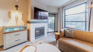 Ein modernes Hotelzimmer mit Kamin, Flachbildfernseher, Sofa und großem Fenster mit Blick ins Freie.