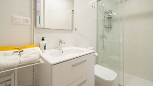 Un baño moderno con ducha de vidrio, un lavamanos blanco y un espejo sobre él.