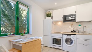 Cocina compacta con microondas, horno, lavadora y un pequeño comedor con mesa y sillas.