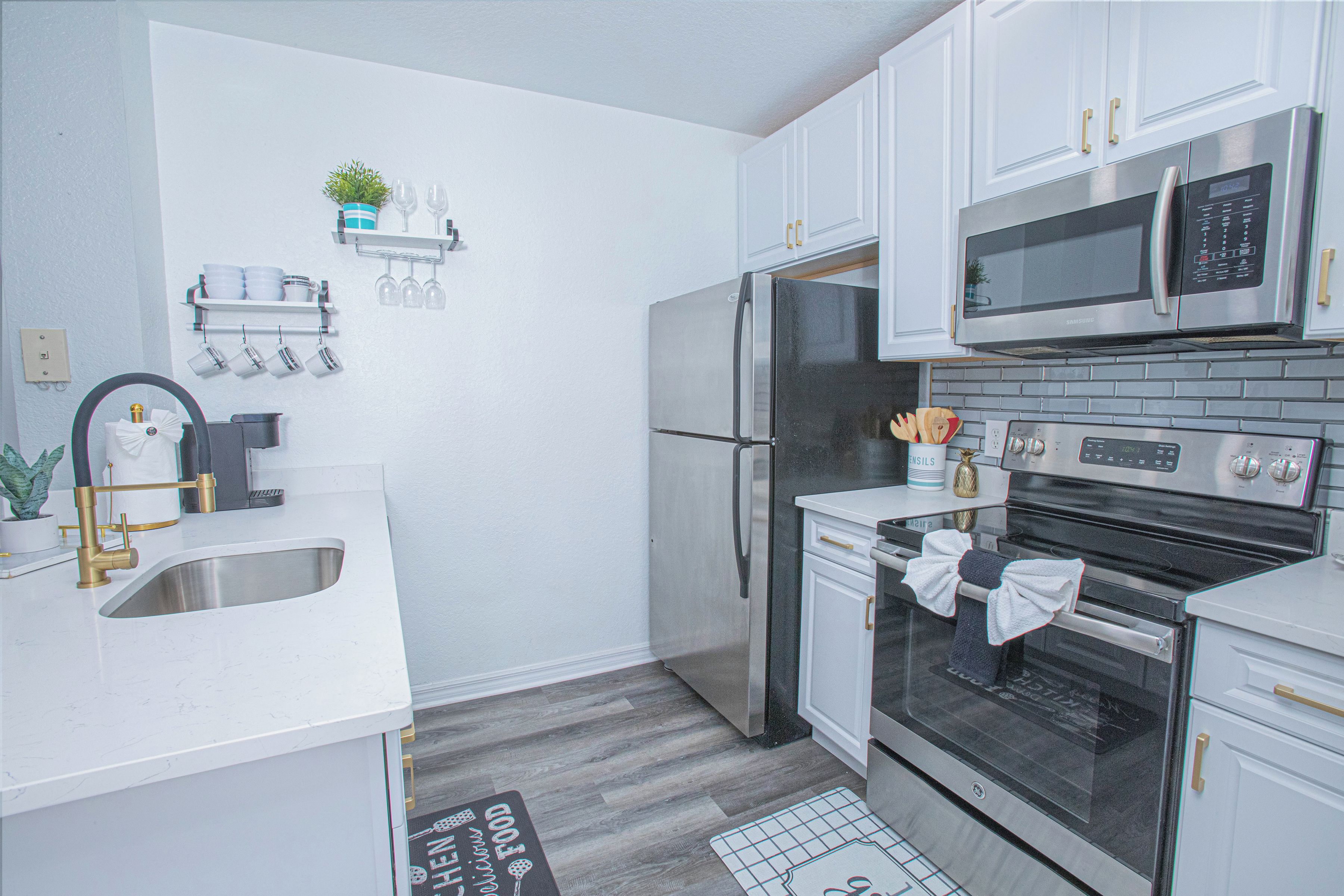 A modern kitchen with stainless steel appliances, white cabinetry, and a small potted plant on the wall.