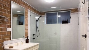 Bagno con una cassettiera bianca, box doccia in vetro e specchio con parete a parete in mattoni.