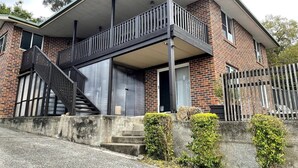 Una casa a due piani in mattoni con un balcone, una scala e un vialetto in cemento.
