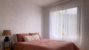 Una camera da letto con un letto, una lampada e una finestra con tende leggere.