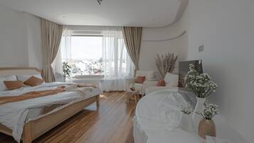 Ein modernes Schlafzimmer mit einem hölzernen Bett, einem weißen Sofa und Blick auf die Stadt durch transparente Vorhänge.