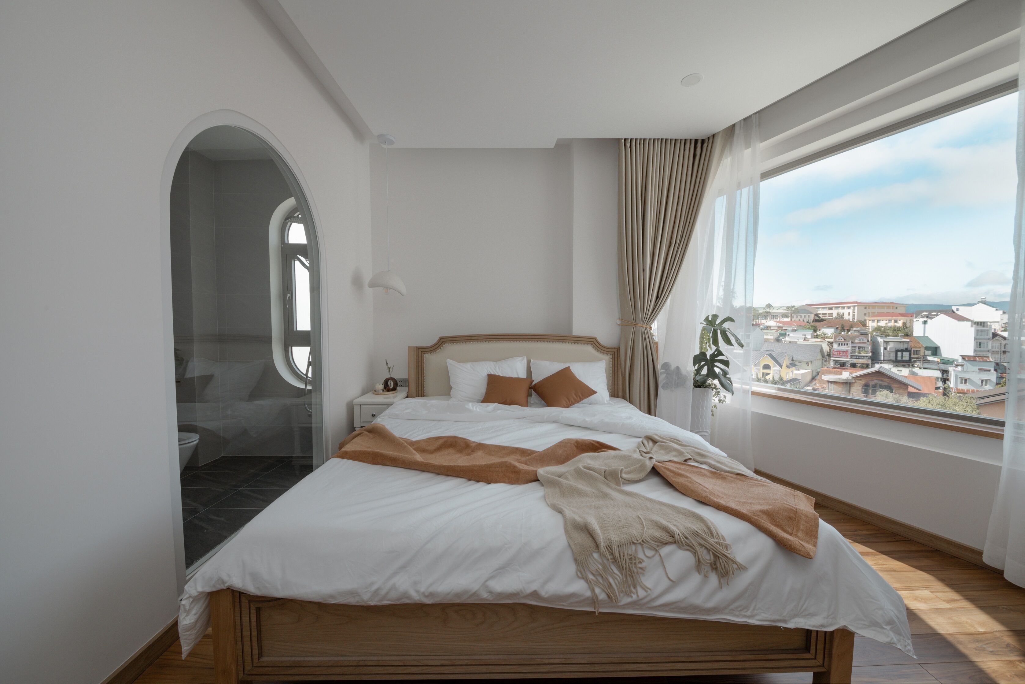 Ein Schlafzimmer mit einem großen Bett, einem Fenster mit Blick auf Gebäude und einer Tür zu einem Badezimmer.