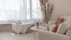A modern living room with a curved sofa, a small round table, and a window with sheer curtains. - Jodi Dalat Hotel (Lam Vien - Da Lat)