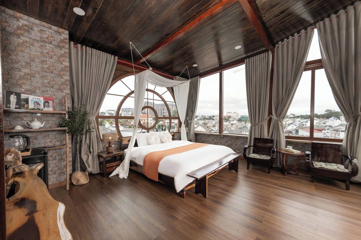 Ein geräumiges Schlafzimmer mit einem großen Bett, Holzboden und Blick auf die Stadt durch große Fenster.