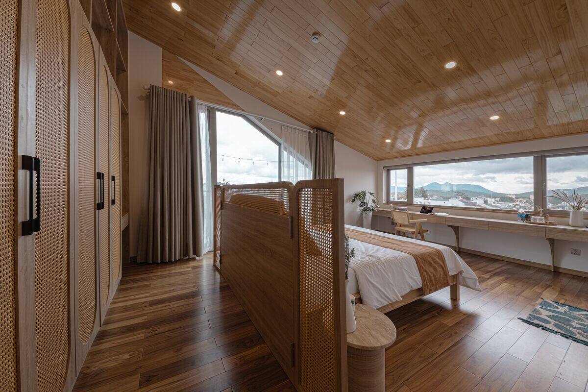 Ein modernes Schlafzimmer mit Holzbalkendecke, einem großen Fenster mit Aussicht, einem Bett, einem Schreibtisch und einem begehbaren Kleiderschrank.