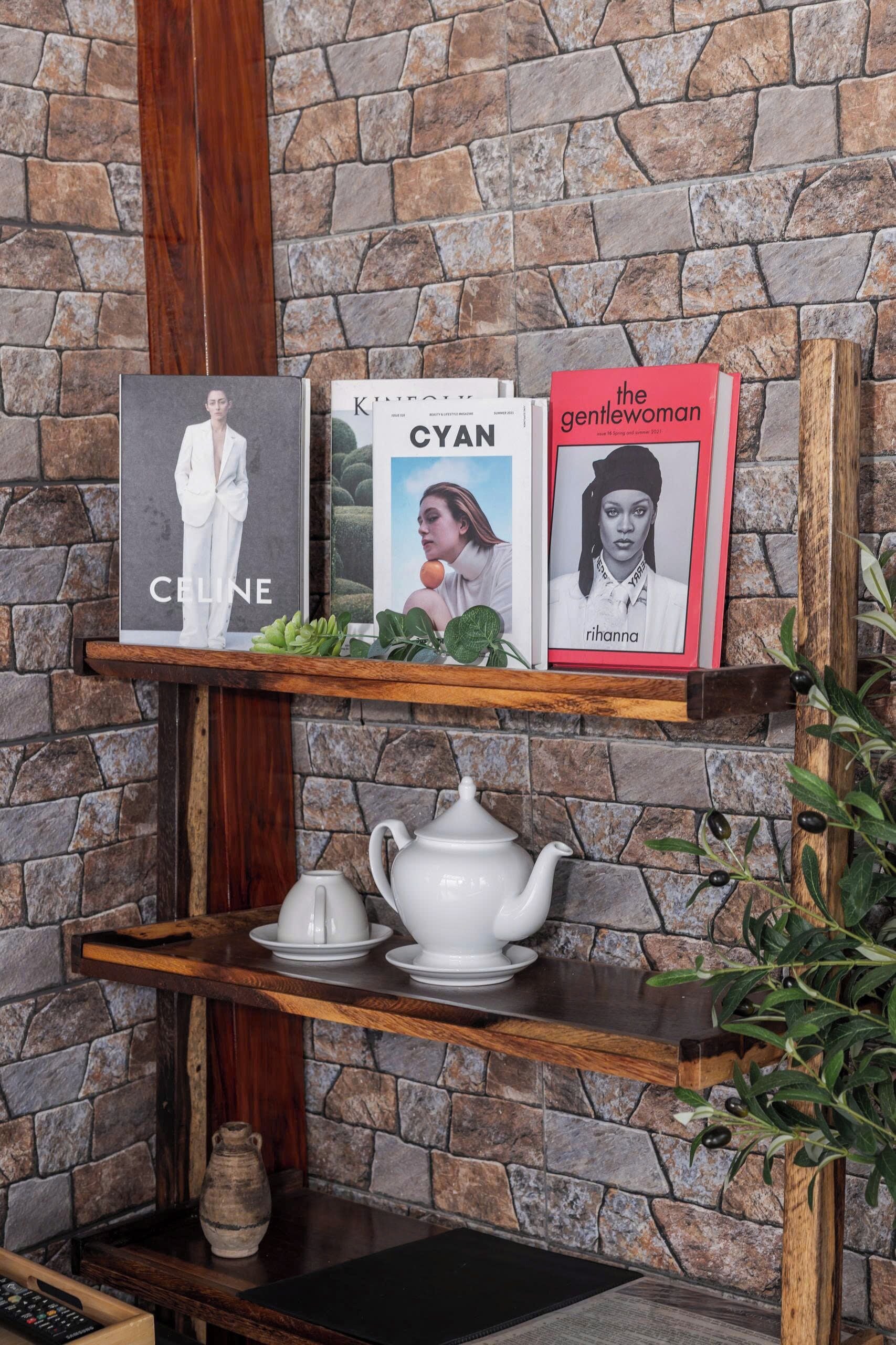 A shelf with books and a teapot against a stone wall.