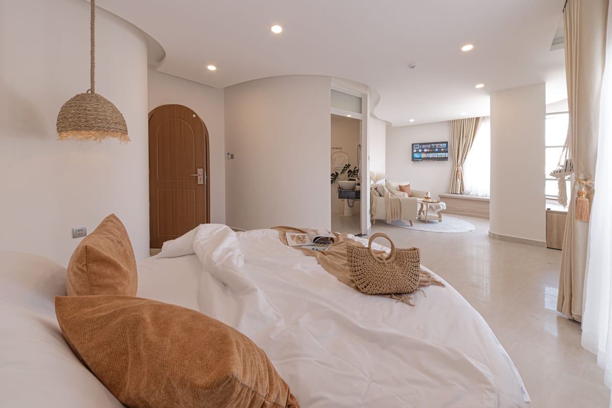 Ein modernes Hotelzimmer mit einem großen Bett, einer Holztür, einem Fernseher und einem durch eine geöffnete Tür einsehbaren Badezimmer.