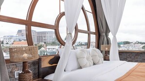 A bedroom with a large window, a bed with white bedding, a wooden headboard, and a nightstand with a lamp. - Jodi Dalat Hotel (Lam Vien - Da Lat)