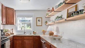 A kitchen with wooden cabinets, a marble countertop, and a window with a view of greenery. - Peaceful + Private Designer Home - Great Location! (Spokane)