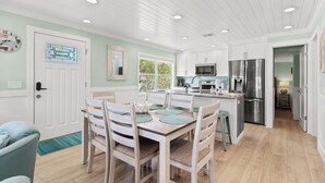 Una cocina moderna con armarios blancos, electrodomésticos de acero inoxidable y un comedor con sillas y una mesa de madera.