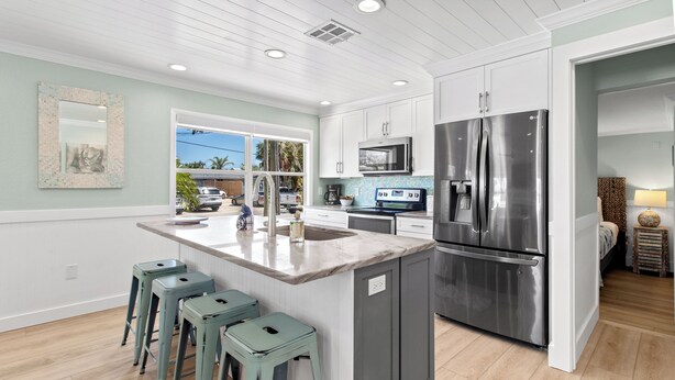 Una cocina moderna con armarios blancos, un refrigerador de acero inoxidable y una isla grande con taburetes de bar.