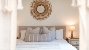 A neatly made bed with a headboard, a bedside lamp, and a wall-mounted circular mirror.