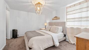 A bedroom with a bed, a nightstand, a lamp, a chandelier, and a window with curtains.