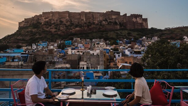A table with plates and a lamp, overlooking a historic fort and a densely packed town. - Zostel Jodhpur - Clock Tower (Jodhpur)