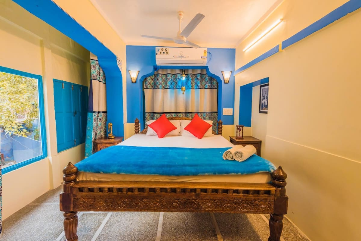 Un dormitorio con cama, ventilador de techo, aire acondicionado y ventana con cortinas.