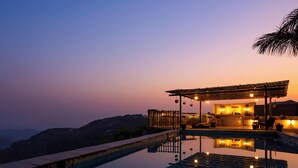 A poolside area with a wooden deck, a covered seating area, and a view of the surrounding landscape. - Zostel Banikhet (Dalhousie)