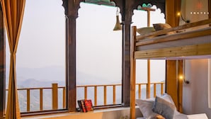 A cozy room with a bunk bed, a window with a view of mountains, and a small plant on the windowsill. - Zostel Banikhet (Dalhousie)
