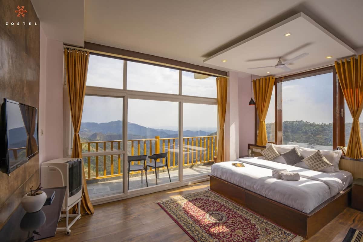 Een slaapkamer met een groot bed, uitzicht op bergen, een balkon met stoelen en een plafondventilator.