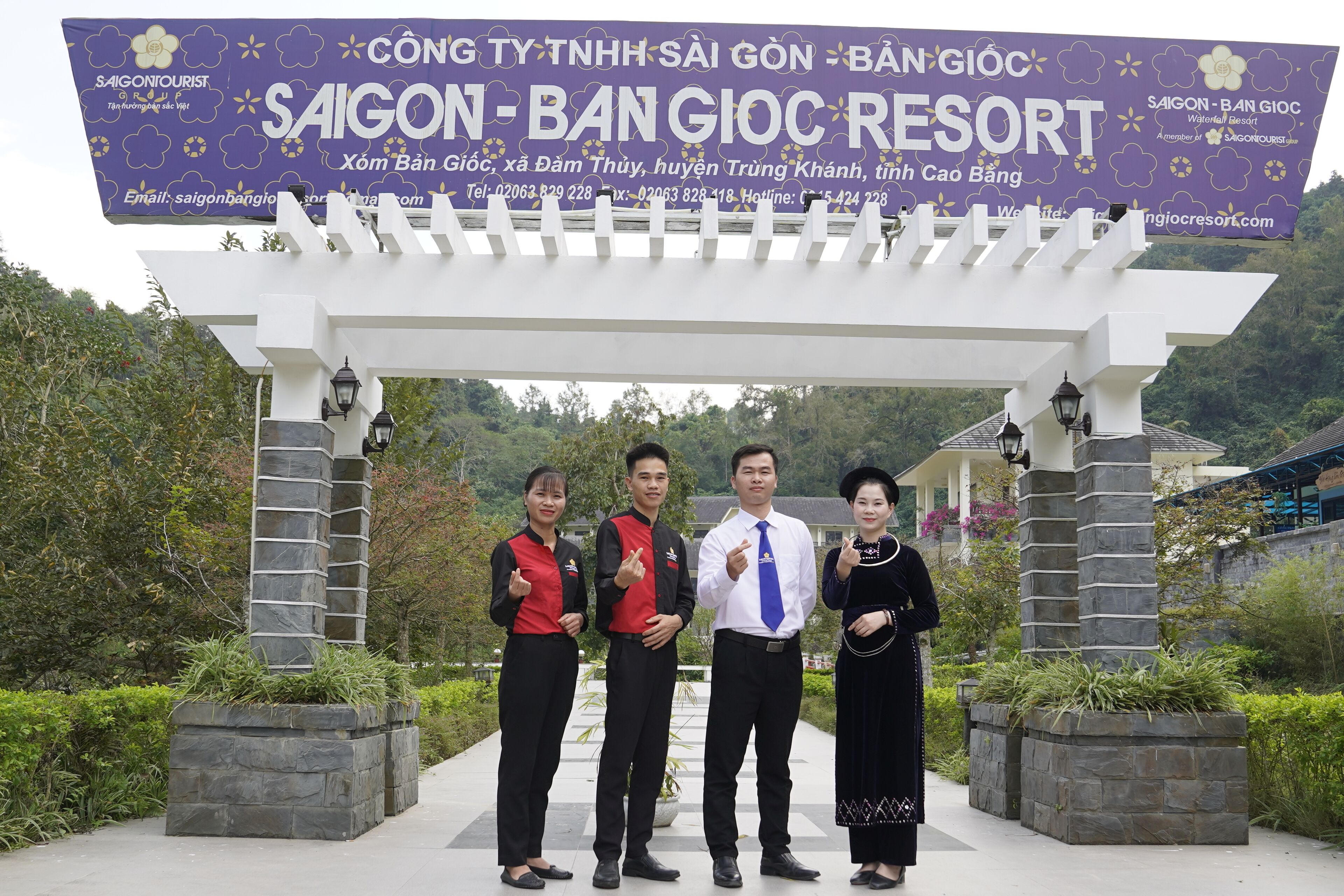 A group of people standing under a pergola with a banner for Saigon-Bang Gioc Resort.