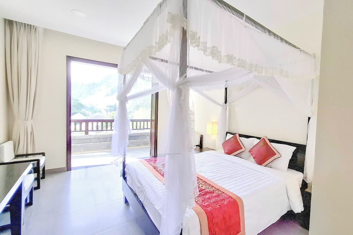 Une chambre d’hôtel avec un lit à baldaquin, un bureau et un balcon offrant une vue.