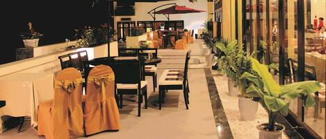 An outdoor dining area with tables and chairs, some covered with yellow chairs, and potted plants.