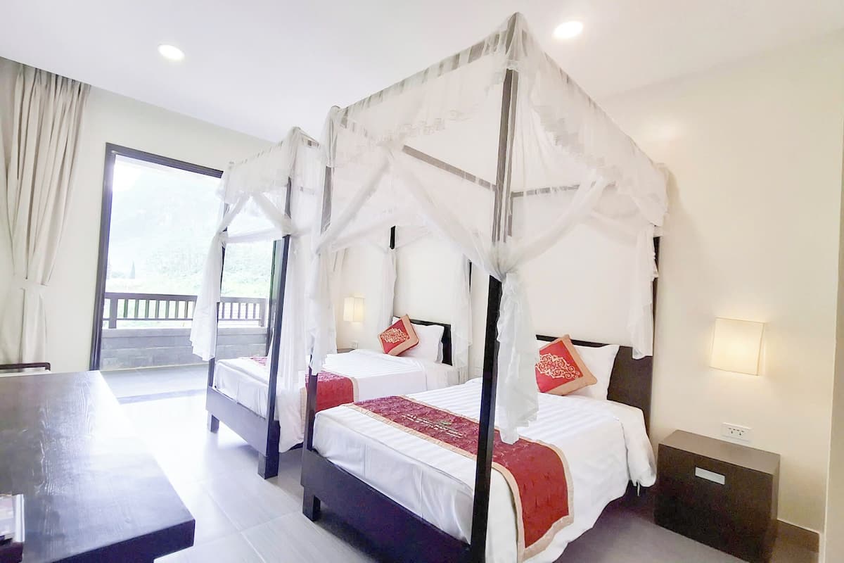 Un lit à baldaquin à quatre poteaux, avec une literie blanche et des touches de rouge, une télévision et un bureau avec une chaise, dans une chambre d’hôtel.