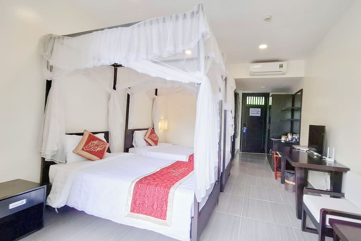 Une chambre d’hôtel avec un lit à baldaquin, un bureau et une chaise. Une porte donne sur le couloir.