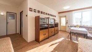 A spacious living area with a wooden cabinet, a dining table with chairs, and a large window providing natural light.