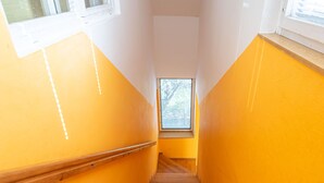 A staircase with wooden steps and yellow walls, leading to a window with a view of trees.