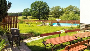 A backyard with a swimming pool, picnic tables, a barbecue grill, and a swing set.