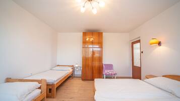 A room with two single beds, a wooden wardrobe, a purple chair, and a wall-mounted lamp.
