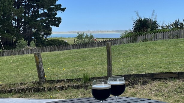 Ein Holztisch mit zwei Weingläsern auf einer Terrasse mit Blick auf ein Wiesenfeld und einen Holzzaun.