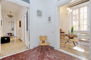 A spacious room with a wooden chair, a dining table with chairs, and a large window with natural light.