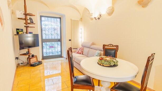 A dining area with a round table, chairs, a sofa, and a TV on a stand.