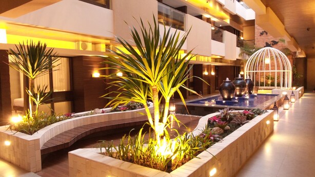 A modern hotel lobby with a central water feature, potted plants, and a seating area with a glass enclosure. - Sweet Garden Guest House (Malang)