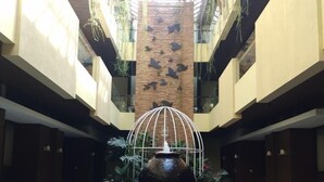 A central atrium with a swimming pool, a large decorative fountain, and a modern architectural design with balconies and plants. - Sweet Garden Guest House (Malang)
