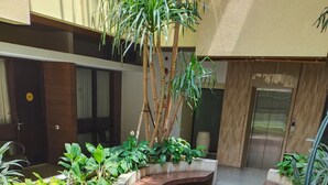 A courtyard with curved planters containing various plants, a tiled floor, and a building entrance with an elevator. - Sweet Garden Guest House (Malang)