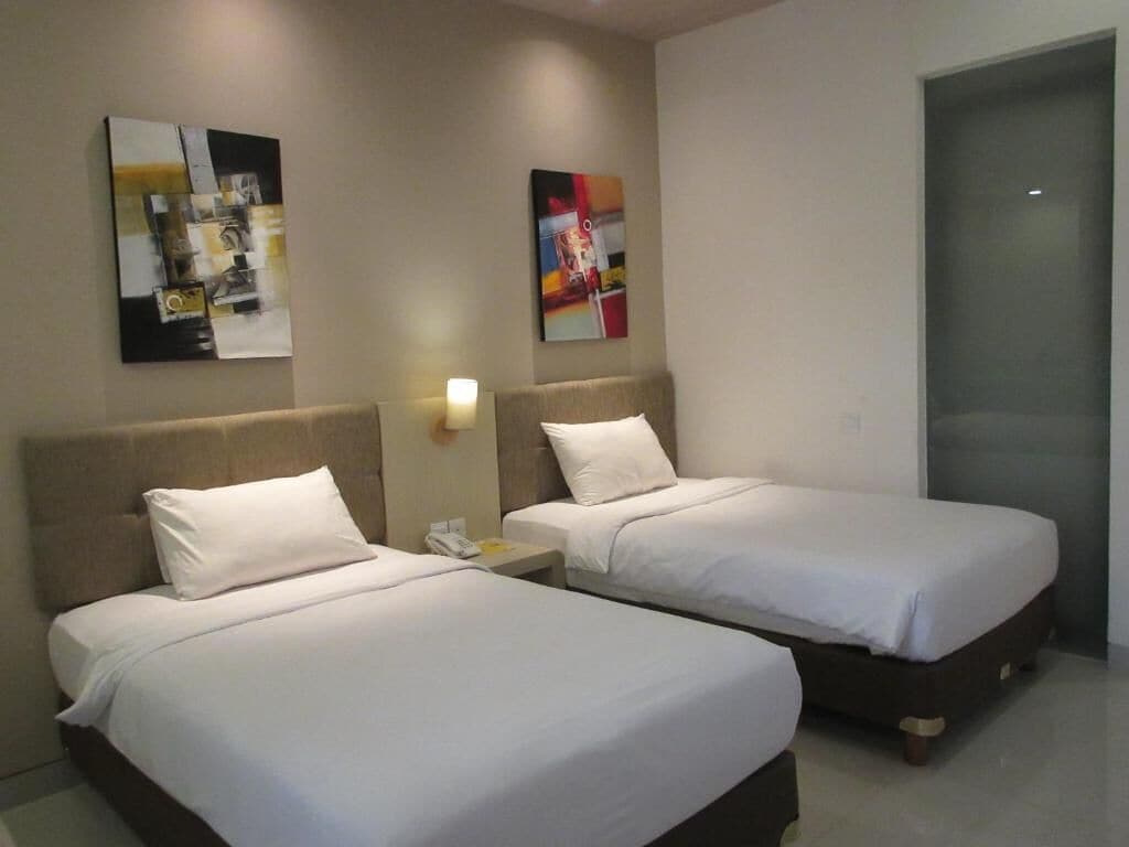 A hotel room with two beds, a nightstand with a phone, and abstract art on the walls.