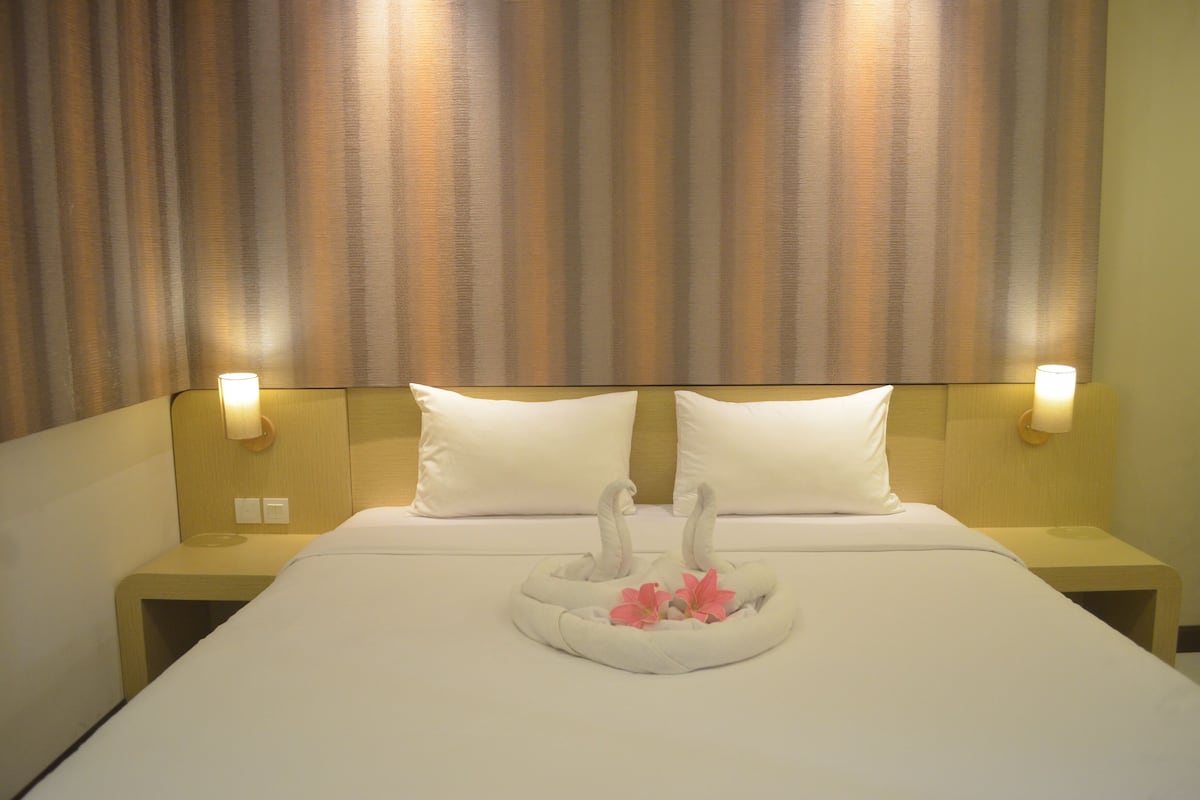 Ein Hotelzimmer mit einem großen Bett, zwei Kissen, Nachttischlampen und einem dekorativen Kopfende in Schwanenform mit Blumen.