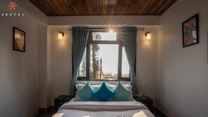 A bedroom with a large bed, a window with curtains, a nightstand, and a framed picture on the wall. - Zostel Rinchenpong (Pelling) (Gyalshing)