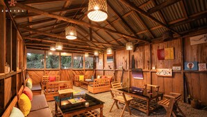 A rustic wooden interior with multiple seating areas, including benches and a table, and a large window providing a view of the outdoors. - Zostel Rinchenpong (Pelling) (Gyalshing)