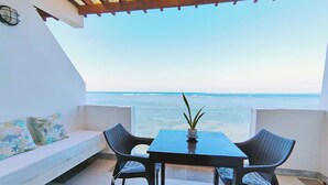 A balcony with a table and chairs, a potted plant, and a view of the sea.
