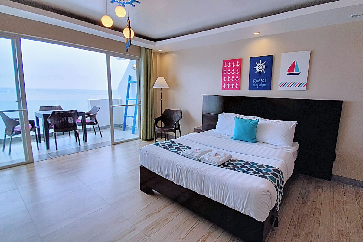 A hotel room with a large bed, a balcony with a table and chairs, and nautical-themed wall decorations.