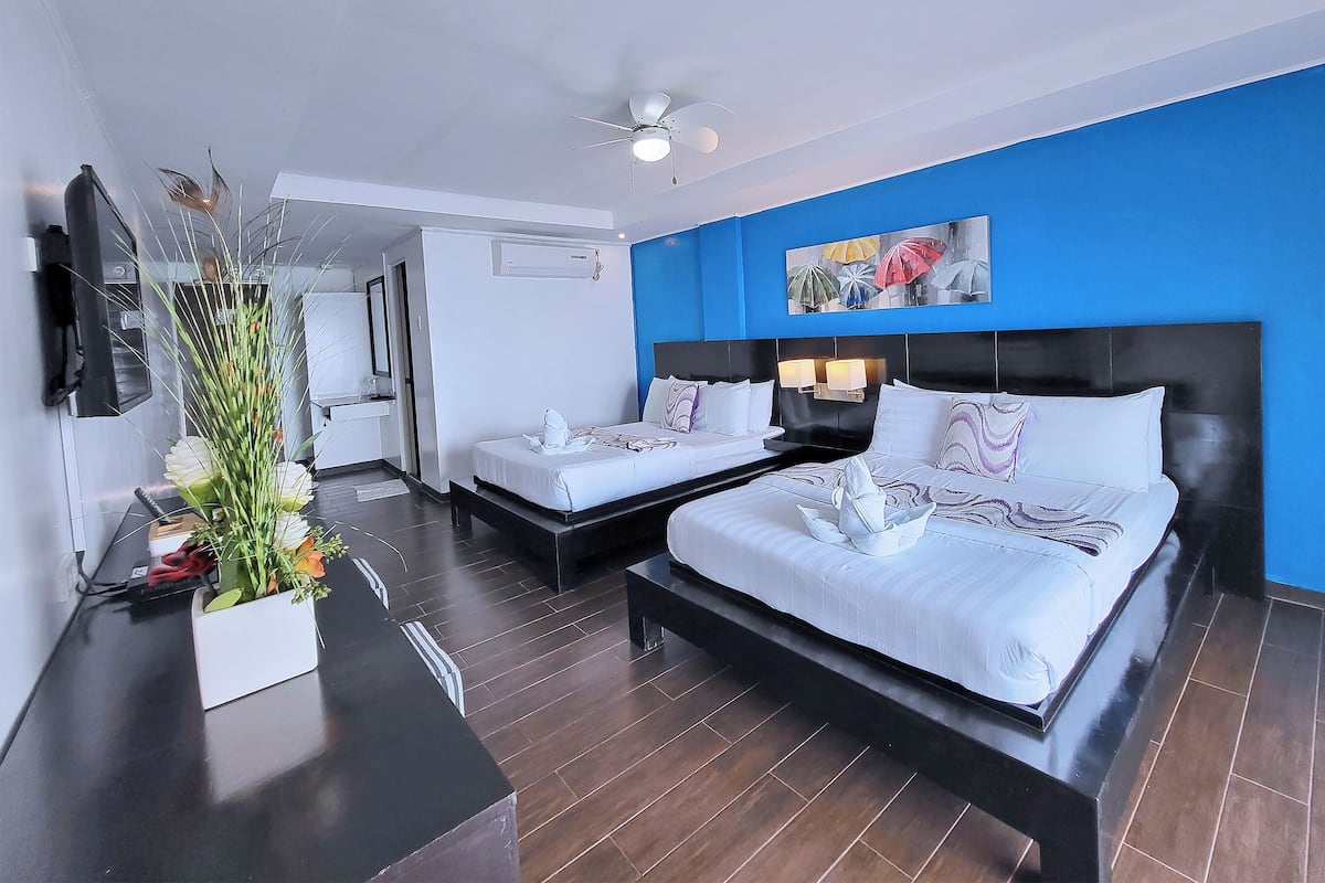 A hotel room with two beds, a large mirror, a ceiling fan, and a painting on the wall.