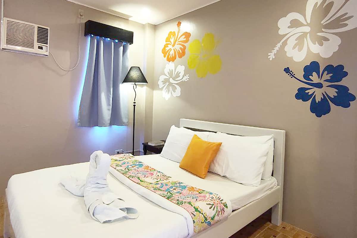 A hotel room with a bed, a nightstand, a lamp, and a wall with floral decorations.