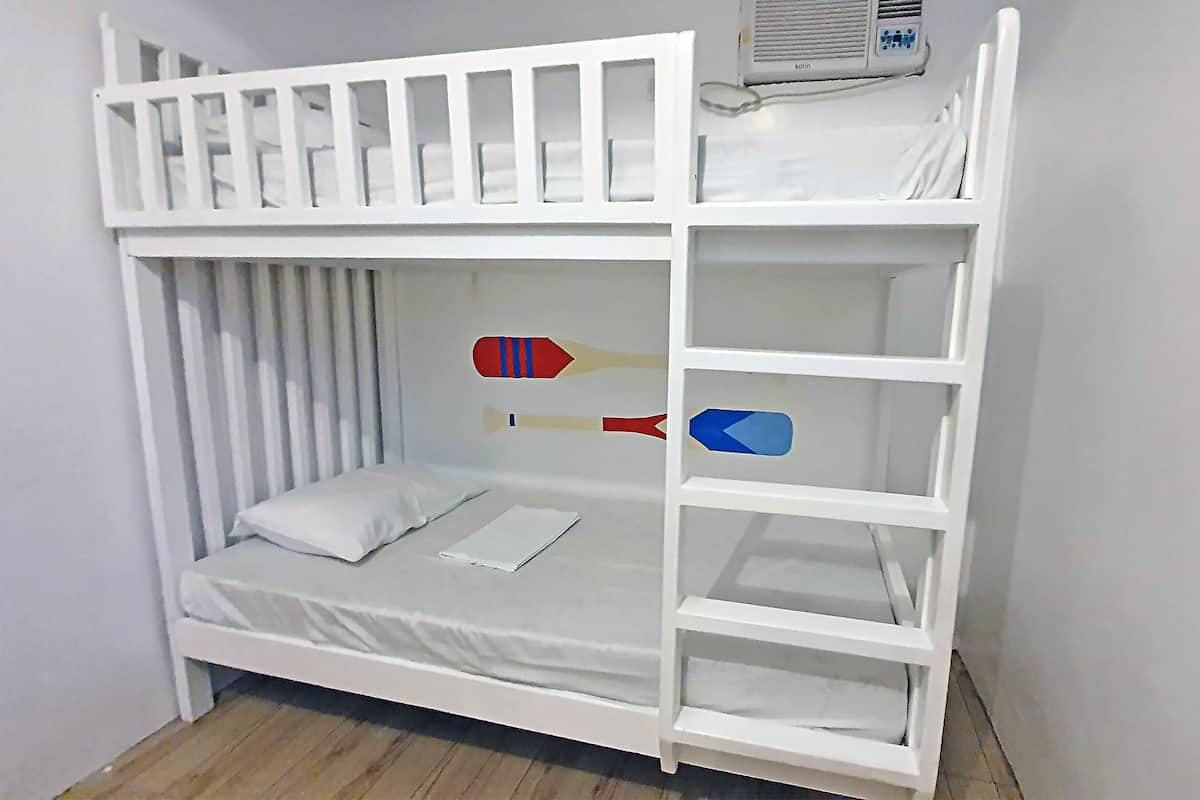 A bunk bed with a white frame, a mattress, and a pillow. There is a small shelf on the side.